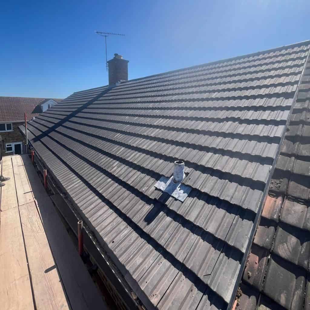 Newly laid grey concrete interlocking tile roof on a house, viewed along the slope with a chimney and clear blue sky.