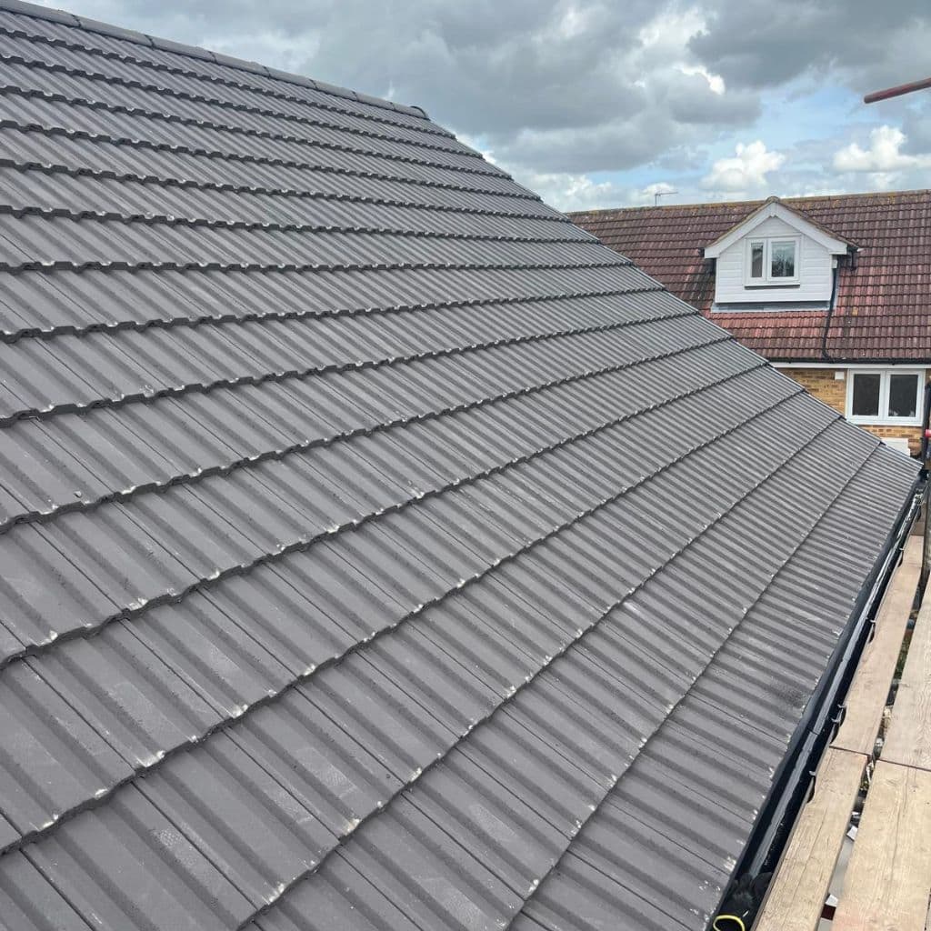 Newly laid grey concrete tile roof on a pitched slope, with scaffolding and neighbouring rooftops beyond.