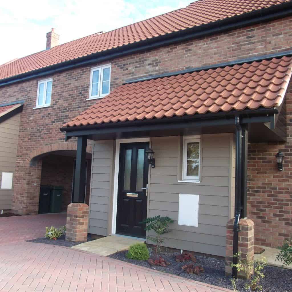 House entrance with grey uPVC weatherboard cladding around the porch, a red tiled canopy and a black front door.