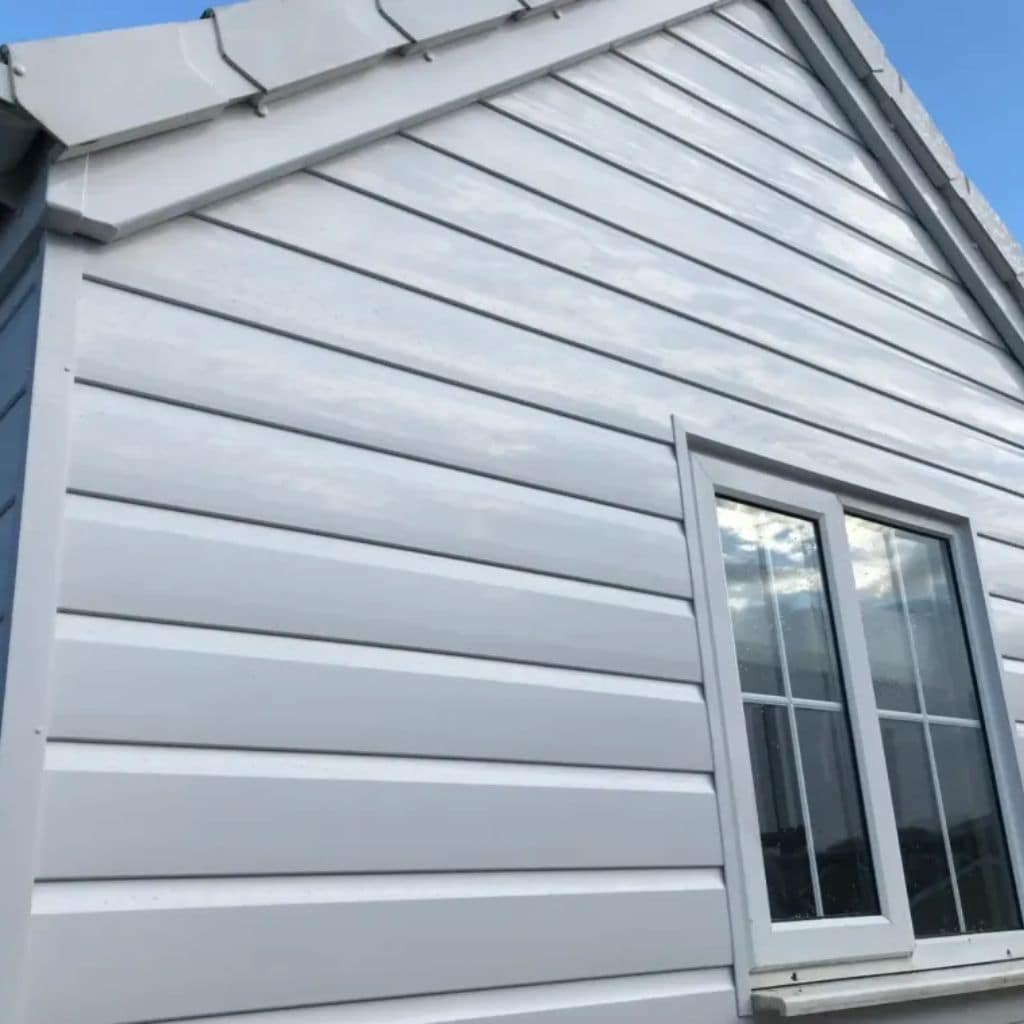 Light grey uPVC shiplap cladding covering a gable wall, with a leaded casement window and grey verge tiles under blue sky.